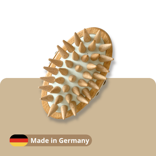 A wooden massage brush with natural wood spikes on a white background, with a beige banner at the bottom featuring a German flag icon and the text 'Made in Germany'.